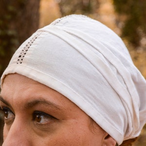 May include: A white cotton head covering with a decorative trim. The head covering is folded and worn on the head.