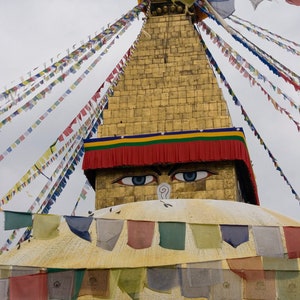 May include: A golden stupa with a red and yellow striped canopy, decorated with colorful prayer flags. The stupa has a pair of eyes painted on the front.