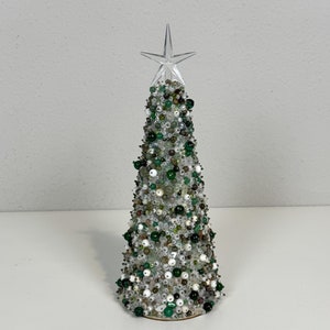 Peut inclure: Un petit sapin de Noël conique en perles de couleur vert, blanc et argent. Le sapin est surmonté d'une étoile en plastique transparent.