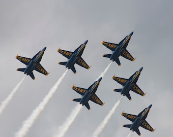 May include: Six blue and yellow fighter jets fly in formation, leaving white smoke trails in the sky. The jets are labeled "U.S. NAVY".