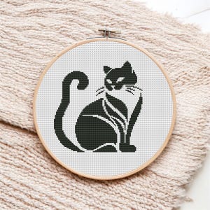 Puede incluir: Silueta negra y blanca de un gato sentado con la cola enroscada alrededor de su cuerpo. El gato está en un aro de bordado de madera.