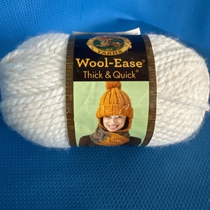 May include: A skein of Lion Brand Wool-Ease Thick & Quick yarn in white with a silver shimmer. The yarn is packaged with a label featuring a woman wearing a knitted hat and scarf in mustard yellow.
