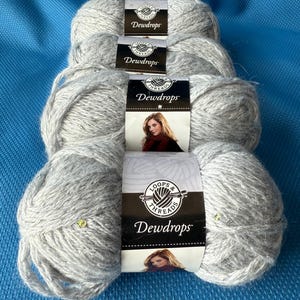Op de afbeelding: Vier strengen grijs garen met het label "Dewdrops" van Loops & Threads. Het garen is lichtgrijs van kleur met een licht getextureerde uitstraling. De labels tonen een vrouw met lang haar en een rode sjaal.