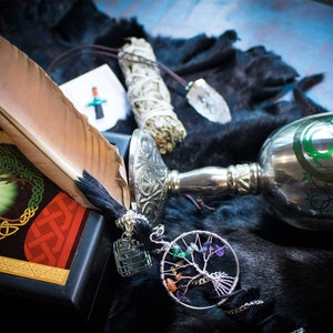 May include: A collection of spiritual and magical items including a feather, a chalice, a sage bundle, a tree of life charm, and a box with a tree of life design.
