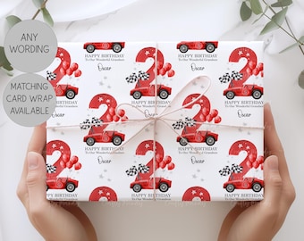 May include: White wrapping paper featuring a repeating pattern of red race cars with the number 2, checkered flags, red balloons, and the text Happy Birthday To Our Wonderful Grandson Oscar. The paper is tied with a thin white string.