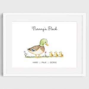 May include: A framed watercolour print featuring a mother duck and three ducklings, with the text "Nanny's Flock." The duck has a green head and brown body. The ducklings are yellow. Names "Harry | Millie | George" are below.