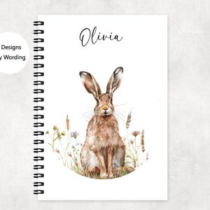 May include: A spiral bound notebook with a watercolor illustration of a brown hare in a field of wildflowers. The name "Olivia" is written at the top of the notebook.