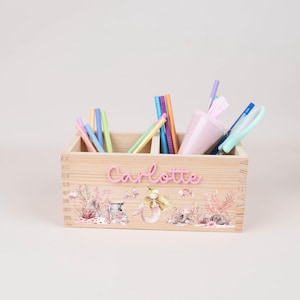 May include: A wooden desk organizer with a mermaid theme. The organizer is filled with pens, pencils, and a pink cup. The name "Charlotte" is displayed in pink letters on the front, with a mermaid and underwater scene.
