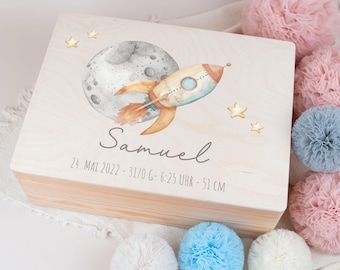 May include: A wooden keepsake box with a white background and a watercolor illustration of a rocket ship flying past the moon. The box has the name "Samuel" and the date "24 MAI 2022 - 3170 G - 6:25 UHR - 51 CM" written on it.