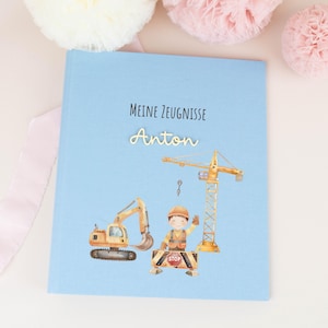 Op de afbeelding: Een lichtblauw hardcover boek met de tekst "Meine Zeugnisse" en de naam "Anton" in script. De kaft toont een aquarelillustratie van een bouwvakker, een gele graafmachine en een gele bouwkraan.