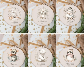 Op de afbeelding: Zes ronde houten ornamenten met verschillende dierillustraties en namen. De ornamenten zijn versierd met een witte achtergrond en gouden sterren. De namen op de ornamenten zijn Julia, Mama, Olga, Oma, Lukas en Maria.