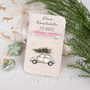 May include: A wooden sign with a pink and white striped ribbon that says "Kleiner Wunschert&uuml;ller f&uuml;r Marco". The sign has a white car with a Christmas tree on top and gold stars in the background.