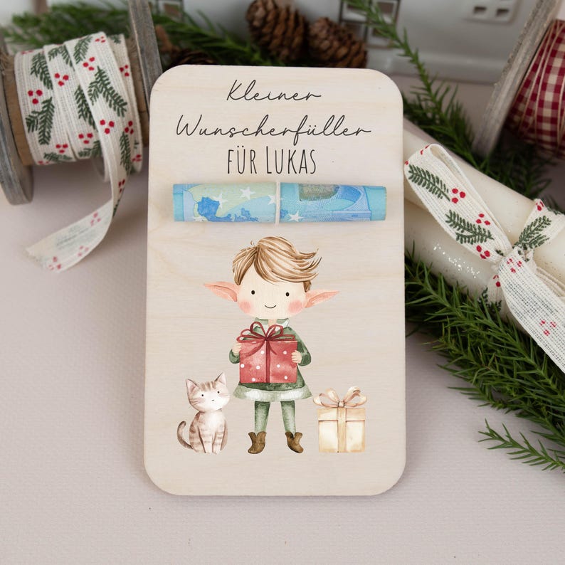 May include: A wooden sign with a watercolor illustration of an elf holding a gift, a cat, and a gift box. The sign says "Kleiner Wunschersch&uuml;ller f&uuml;r Lukas".