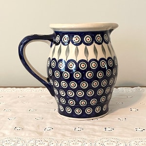 May include: A blue and white ceramic pitcher with a decorative pattern of circles and leaves. The pitcher has a wide mouth and a handle.