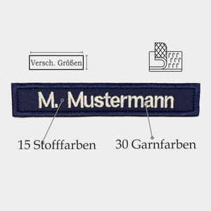 Könnte beinhalten: Ein marineblauer gestickter Aufnäher mit dem Text "M. Mustermann" in weißer Farbe. Der Aufnäher besteht aus 15 Stofffarben und 30 Garnfarben.