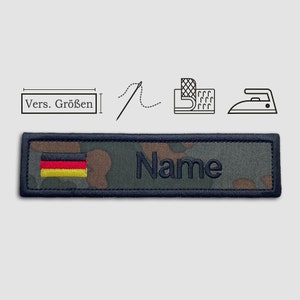 Könnte beinhalten: Ein schwarzer und grüner Tarnstoff-Patch mit einer deutschen Flagge und dem Wort "Name" in schwarzem Faden gestickt. Der Patch kann auf Kleidung oder andere Gegenstände genäht oder gebügelt werden.