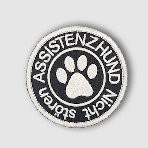Könnte beinhalten: Schwarz-weiß gestickter Aufnäher mit einem Pfotenabdruck in der Mitte und dem Text "Nicht Stören Assistenzhund" am Rand.