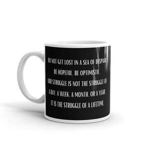 Op de afbeelding: Een witte keramische mok met een zwart ontwerp. De mok heeft een motiverende quote: "RAAK NIET VERLOREN IN EEN ZEE VAN VERWANTWOORDELING. WEES HOOPVOL. WEES OPTIMISTISCH. ONZE STRUGGLE IS NIET DE STRUGGLE VAN EEN DAG. EEN WEEK. EEN MAAND. OF EEN JAAR. HET IS DE STRUGGLE VAN EEN LEVEN."