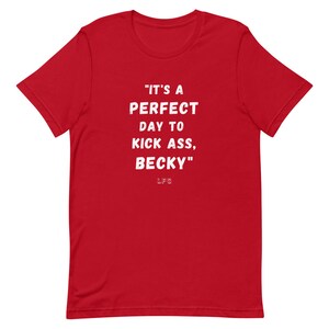 May include: A red t-shirt with white text that reads "IT'S A PERFECT DAY TO KICK ASS, BECKY." The letters "LFG" are below the quote. The shirt has short sleeves and a crew neck.