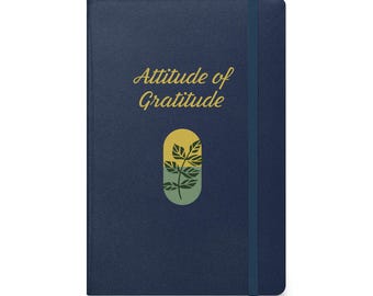 May include: A dark blue notebook with a gold inscription that reads "Attitude of Gratitude". A stylized green plant is depicted in a yellow and green oval shape.