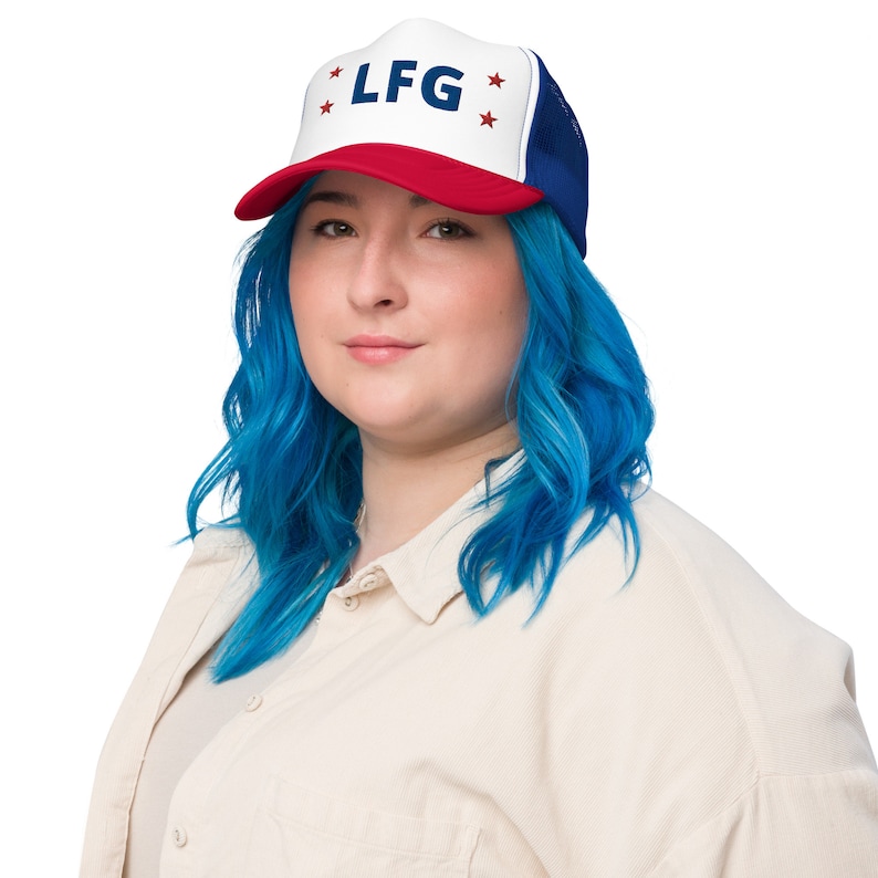 May include: A woman with blue hair is wearing a red, white, and blue trucker hat with the text "LF G" and stars on it.