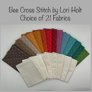 May include: A fan-shaped arrangement of 21 fabric squares with a cross-stitch pattern. The fabrics are in a rainbow of colors, including brown, orange, red, purple, blue, and green. The text "Bee Cross Stitch by Lori Holt Choice of 21 Fabrics" is at the top of the image.
