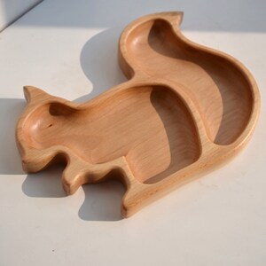May include: A wooden squirrel-shaped plate with two divided sections. The plate is made of natural wood and has a light brown color.