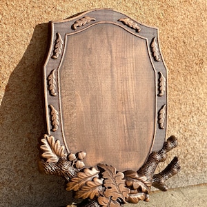 Puede incluir: Una placa de madera con un diseño de hoja de roble tallada. La placa es marrón y tiene una superficie lisa. Es perfecta para exhibir un trofeo o un premio.