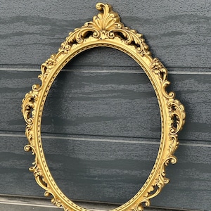 Puede incluir: Un marco de imagen grande, ovalado, de color dorado, con detalles intrincados y un acabado liso y pulido.