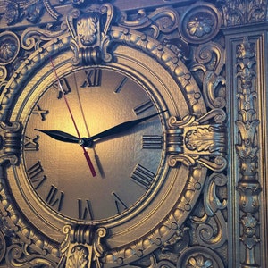 Puede incluir: Un reloj dorado con números romanos y detalles ornamentados. La esfera del reloj está rodeada de tallas intrincadas y un marco decorativo.