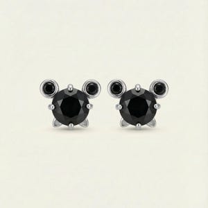 May include: A pair of stud earrings with a central black, round gemstone, flanked by two smaller black stones on each side. The earrings have a silver setting and a post fastening.