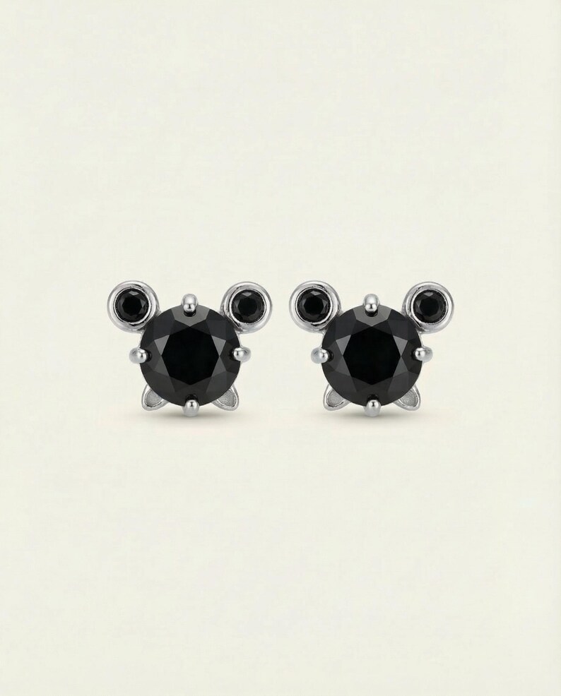 May include: A pair of stud earrings with a central black, round gemstone, flanked by two smaller black stones on each side. The earrings have a silver setting and a post fastening.
