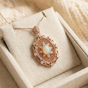 Könnte beinhalten: Halskette mit roségoldfarbenem Anhänger. Der ovale Anhänger hat ein sternförmiges Design mit einem Opal in der Mitte und kleinen Diamanten. Die Halskette wird auf einer neutralen Oberfläche präsentiert. Das Design des Anhängers ist aufwendig und elegant.