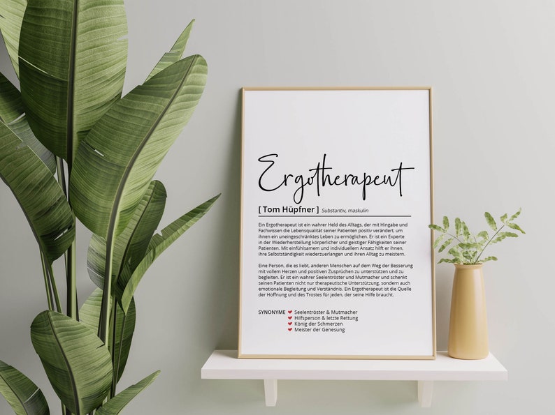 May include: A framed print with a white background and black text. The text reads "Ergotherapent [Tom H&uuml;pfner] Substantiv, maskulin" and a definition of the word. The print is on a white shelf with a green plant and a small vase with a flower on either side.