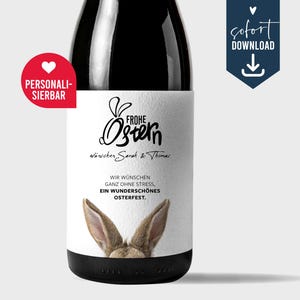 May include: A white wine bottle label with a bunny rabbit peeking out from the bottom. The label says "Frohe Ostern" and "wünschen Sarah & Thomas". The text below the bunny says "Wir wünschen ganz ohne Stress, ein wunderschönes Osterfest."