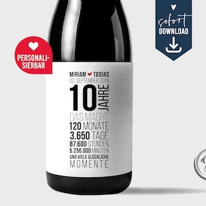 Könnte beinhalten: Eine schwarze Flasche mit einem weißen Etikett. Auf dem Etikett stehen die Namen "Miriam" und "Tobias" sowie das Datum "22. September 2014". Die Zahl "10" ist prominent, mit den Wörtern "Jahre" und "Momente". Ein roter Aufkleber sagt "Personalisierbar".