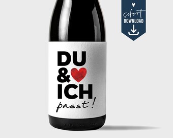 Puede incluir: Una etiqueta de botella de vino blanca con texto negro que dice "DU & ICH passt!" con un corazón rojo entre las palabras "DU" e "ICH".