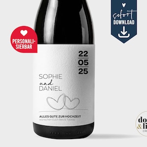 May include: A wine bottle with a white rectangular label featuring the text SOPHIE und DANIEL, the date 22 05 25, and a line-art drawing of two hearts. The label includes the text ALLES GUTE ZUR HOCHZEIT, wünchen Euch Bea & Tobias.