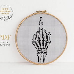 Op de afbeelding: Een kruissteekpatroon van een skelet hand die de middelvinger opsteekt. Het patroon is in een houten borduurring.