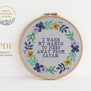 May include: A cross stitch pattern featuring a floral wreath with the text "I wash my hands to keep away from Satan".