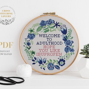 Könnte beinhalten: Ein Kreuzstichmuster mit einem floralen Kranzdesign und dem Text "Willkommen im Erwachsenenalter Hoffentlich magst du Ibuprofen".