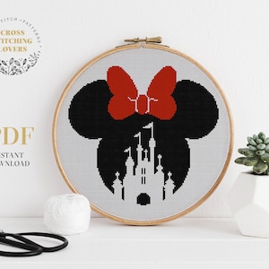 Peut inclure: Un motif de point de croix représentant une silhouette noire et blanche de Mickey Mouse avec un nœud rouge et un château derrière lui. Le motif est dans un cercle de broderie en bois.