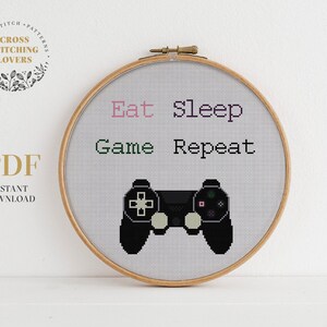 May include: A cross stitch pattern featuring a video game controller and the text "Eat Sleep Game Repeat".