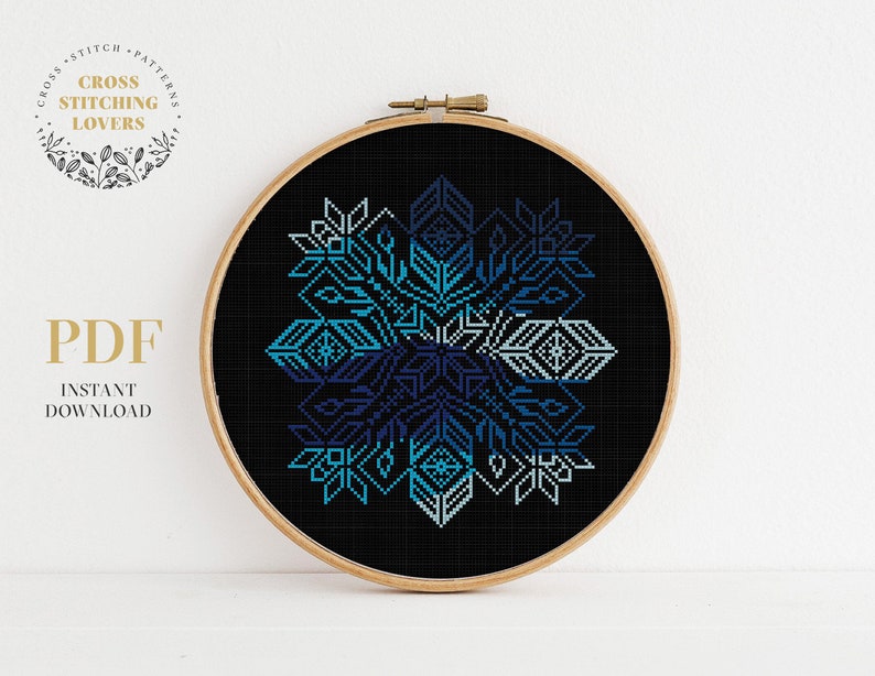 May include: A blue and white geometric snowflake cross stitch pattern on black fabric in a round wooden embroidery hoop.