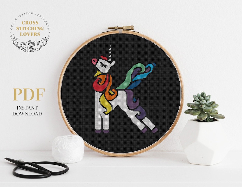 May include: A rainbow unicorn cross stitch pattern in a wooden embroidery hoop. The unicorn is standing on a black background. The pattern is available as a PDF download.