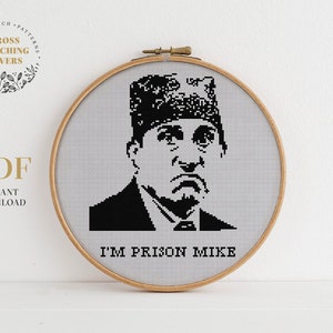 May include: A black and white cross stitch pattern of Michael Scott from The Office TV show. The pattern features Michael Scott wearing a hat and a serious expression. The text "I'm Prison Mike" is below the image.