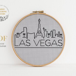 Könnte beinhalten: Ein Kreuzstichmuster der Skyline von Las Vegas, mit den ikonischen Gebäuden und dem Text "LAS VEGAS". Das Muster ist in einem hölzernen Stickrahmen dargestellt.
