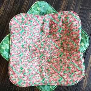 May include: A green and pink fabric bowl with a watermelon print. The bowl is made of two layers of fabric and has a scalloped edge.