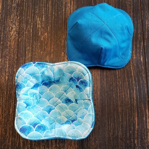 May include: Two blue fabric bowl cozies. One is solid blue and the other has a blue and white scale pattern.