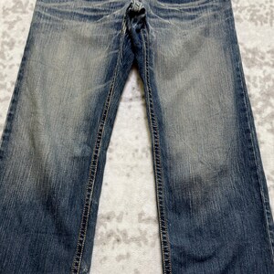 May include: Faded blue denim jeans with a classic five-pocket design. The jeans have a straight leg cut and feature visible stitching along the seams and pockets. The denim has a worn, distressed appearance.